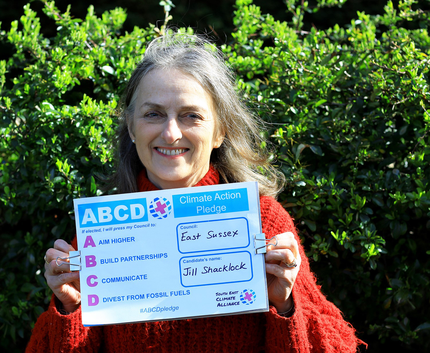 Jill Shacklock holding up the ABCD Climate Action Pledge to Aim Higher, Build Partnerships, Communicate, Divest from Fossil fuels